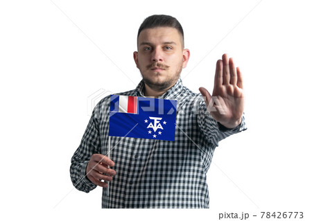 White guy holding a flag of French Southern and Antarctic Territories and with a serious face shows a hand stop sign isolated on a white background White guy holding a flag of French Southern and Antarctic Territories and with a serious face shows a hand stop sign isolated on a white background 78426773