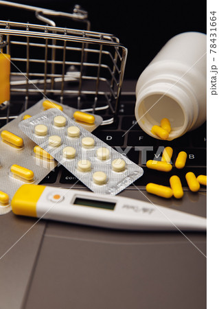 Online shopping with home delivery. Trolley with pills on laptop keyboard and medical tools. Vertical image 78431664