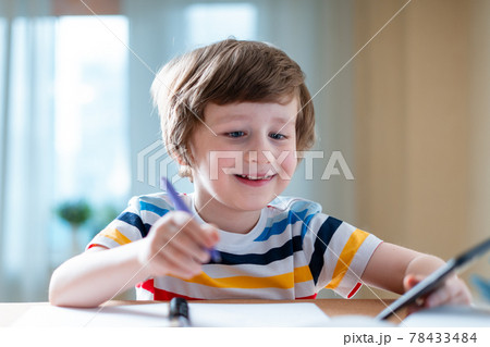 Back to school. Distance learning online education. Caucasian smile kid boy studying at home with smartphone and doing school homework. Smiling child siting at table with cell phone Back to school. Distance learning online education. Caucasian smile kid boy studying at home with smartphone and doing school homework. Smiling child siting at table with cell phone 78433484