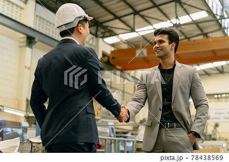 30s young Asian businessman in formal suit and hard hat showing foreign business partner in factory background. Business partnership and team work success concept 30s young Asian businessman in formal suit and hard hat showing foreign business partner in factory background. Business partnership and team work success concept 78438569