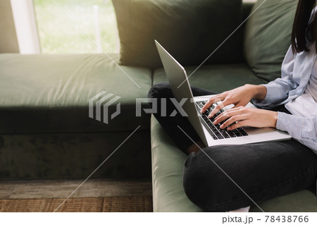 A brunette girl sits on a green sofa and prints something on a laptop 78438766