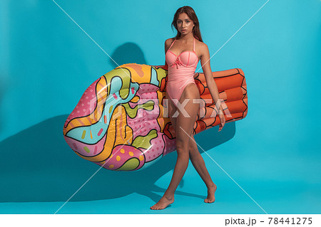 Girl in swimsuit walking on blue background with inflatable mattress 78441275
