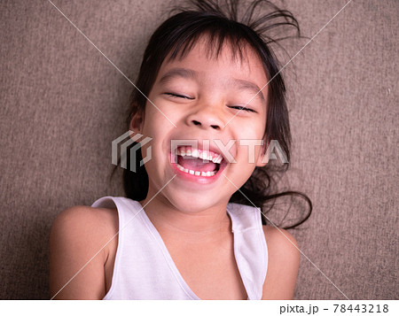 Cute little girl lying on sofa in the living room, looking at camera and smiling while playing at home. Cute little girl lying on sofa in the living room, looking at camera and smiling while playing at home. 78443218
