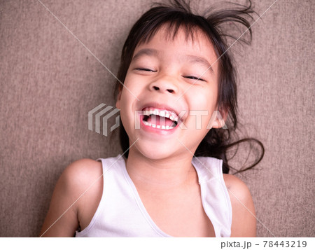 Cute little girl lying on sofa in the living room, looking at camera and smiling while playing at home. 78443219
