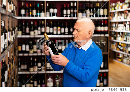 Elderly man chooses red wine in a liquor store 78444938