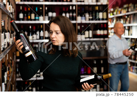 Focused woman customer buying bottle of wine Focused woman customer buying bottle of wine 78445250