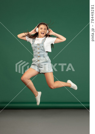 Caucasian woman with headphones jumping over green studio background with copyspace Caucasian woman with headphones jumping over green studio background with copyspace 78449281
