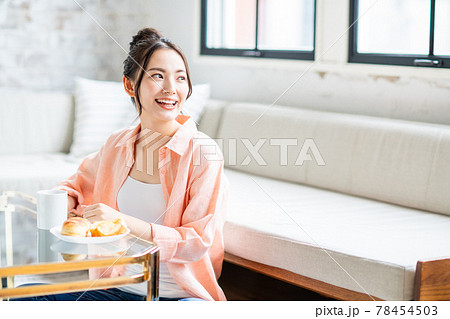 リビングで朝食にコーヒーとデニッシュを食べる若い女性 リビングで朝食にコーヒーとデニッシュを食べる若い女性 78454503