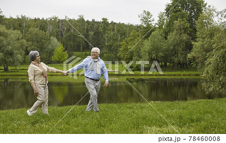 Happy senior man and woman walking by the river in a green park on a fine summer day 78460008