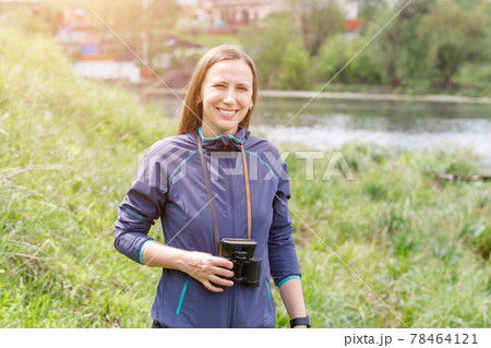 Young woman standing with binoculars near the pond 78464121