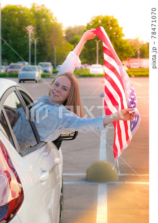 Young millennial blonde woman looking from car with american flag. Flag of the united states in her hands. July 4th Independence Day. USA national holiday. Freedom and memorial concept 78471070