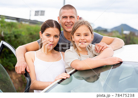 Man, woman and girl standing near car 78475238