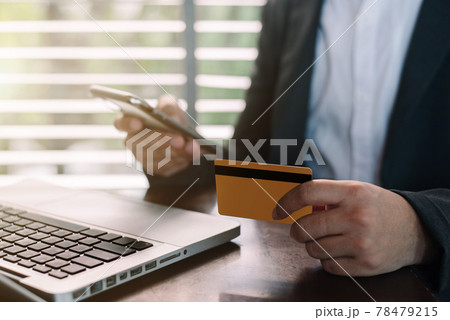 Male use credit cards to conduct financial transactions through phones and laptop in the office. 78479215