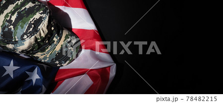 Military hat or bag laying with american flag. Soldier hat or helmet with national american flag on black background. Represent military concept by camouflage object and USA nation flag. Military hat or bag laying with american flag. Soldier hat or helmet with national american flag on black background. Represent military concept by camouflage object and USA nation flag. 78482215