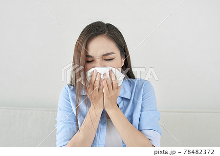 Picture of a sick young lady sitting on the couch and blowing her runny nose Picture of a sick young lady sitting on the couch and blowing her runny nose 78482372