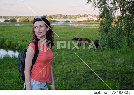 Girl with a backpack, green meadow, two horses in the background. Girl with a backpack, green meadow, two horses in the background. 78482887