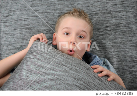 Cute funny boy is lying his backs on couch and making funny face, playful child boy having fun at home. 78482888