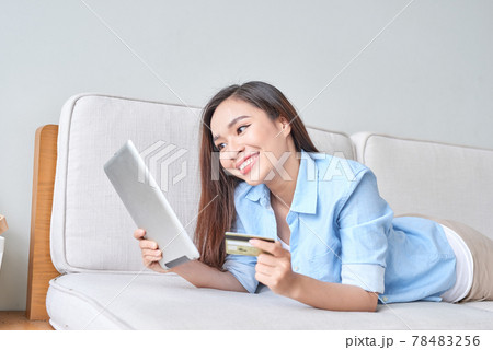 happy woman using digital tablet for online shopping with credit card in the living room 78483256