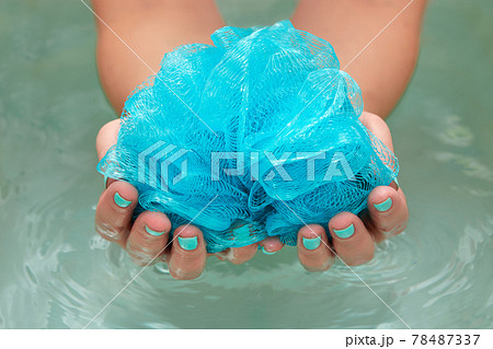 female hands holding a round soft synthetic washcloth in bath with water. Hands close-up. Spa treatment, body care, water background 78487337