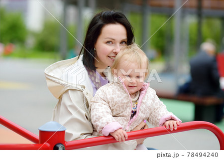 Toddler girl having fun on outdoor playground. Happy young mother rides daughter on carousel. Spring/summer/autumn active leisure for family with kids. Toddler girl having fun on outdoor playground. Happy young mother rides daughter on carousel. Spring/summer/autumn active leisure for family with kids. 78494240