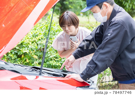 ロードサービスの作業員と故障した車のボンネットをあけて中を確認する女性 78497746