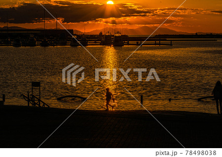 太陽が沈む夕景の波止場に佇む人影と遠景 78498038