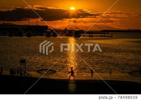 太陽が沈む夕景の波止場に佇む人影と遠景 78498039