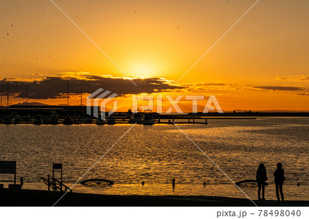 太陽が沈む夕景の波止場に佇む人影と遠景 78498040