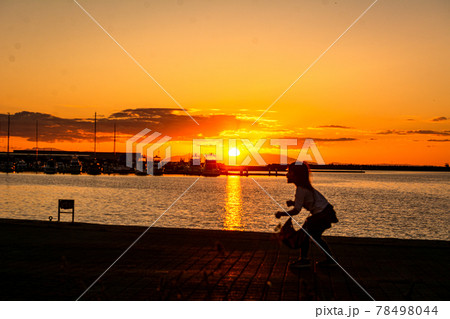 太陽が沈む夕景の波止場に佇む人影と遠景 78498044