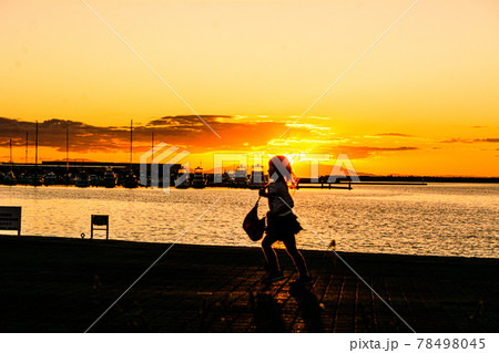 太陽が沈む夕景の波止場に佇む人影と遠景 78498045