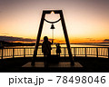 太陽が沈む夕景の波止場に佇む人影と幸せの鐘 78498046