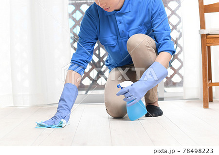 部屋で床掃除をする清掃業の作業服の若い男性 78498223