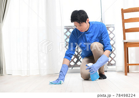 部屋で床掃除をする清掃業の作業服の若い男性 78498224