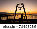 太陽が沈む夕景の波止場に佇む人影と幸せの鐘 78498236