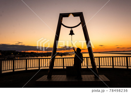 太陽が沈む夕景の波止場に佇む人影と幸せの鐘 78498236