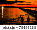 太陽が沈む夕景の波止場に向かう船と佇む人影と遠景の釣り人 78498238