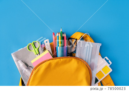 School supplies and medical mask with an antiseptic sticking out of backpack on blue background School supplies and medical mask with an antiseptic sticking out of backpack on blue background 78500023