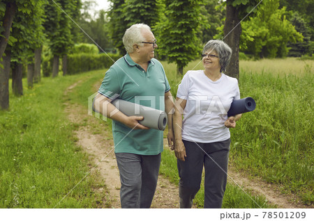 Happy senior couple with yoga mats walking along park path after sports workout in nature 78501209