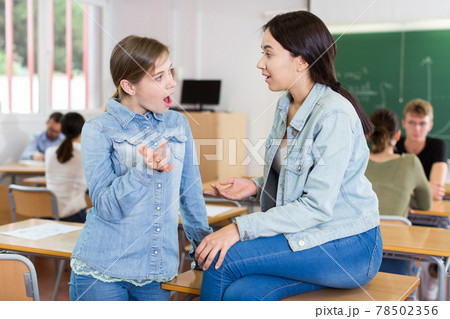 Young girls are sitting at the desk and talking about boys in the classroom 78502356