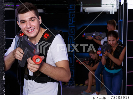 Excited guy holding laser pistol, playing laser tag with friends in dark room 78502913