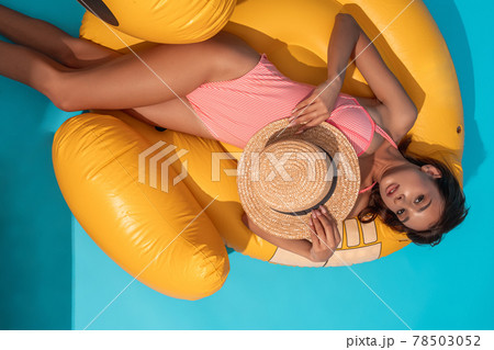 Girl in bathing suit with wicker hat lying on yellow inflatable pool float 78503052