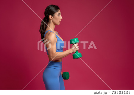 Girl performing arm exercises with dumbbells on maroon background 78503135