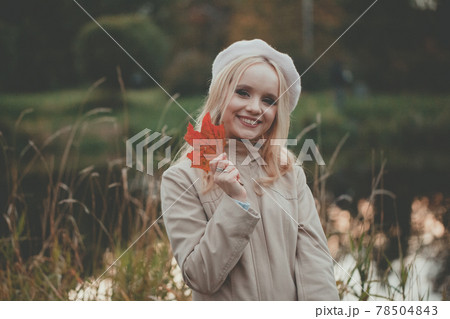 Attractive happy woman with a smile holds an autumn red maple leaf near the face 78504843