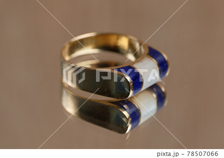 Creative golden ring with blue and white stone on a glass table. Creative golden ring with blue and white stone on a glass table. 78507066