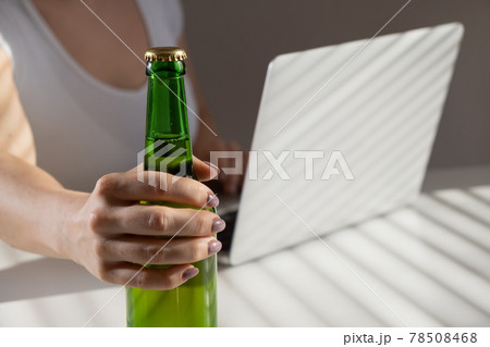 Caucasian woman works at a laptop and drinks beer from a glass bottle 78508468