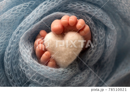 Two cute tiny baby feet wrapped in a blue-green aqua knitted blanket. And a knitted heart made of woolen threads. Two cute tiny baby feet wrapped in a blue-green aqua knitted blanket. And a knitted heart made of woolen threads. 78510021