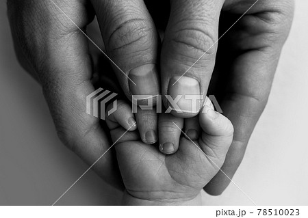 A newborn holds on to mom's, dad's finger. Hands of parents and baby close up. A child trusts and holds her tight. Black and white photo. A newborn holds on to mom's, dad's finger. Hands of parents and baby close up. A child trusts and holds her tight. Black and white photo. 78510023