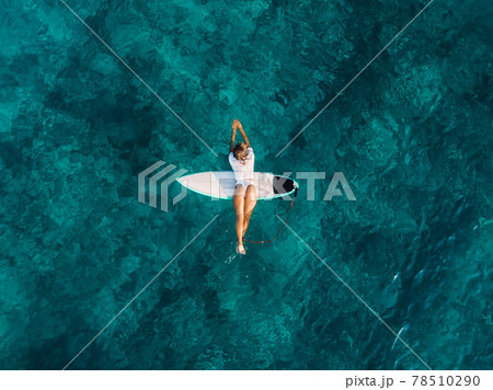 Attractive surf girl relaxing on surfboard in transparent ocean. Aerial view with surfer woman Attractive surf girl relaxing on surfboard in transparent ocean. Aerial view with surfer woman 78510290