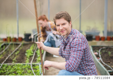 Friendly man with rake crouched near seedlings in greenhouse Friendly man with rake crouched near seedlings in greenhouse 78511084