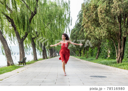 Happy beautiful young woman dancing of freedom in summer park with trees in the background. Asian woman in red dress running of happiness 78516980